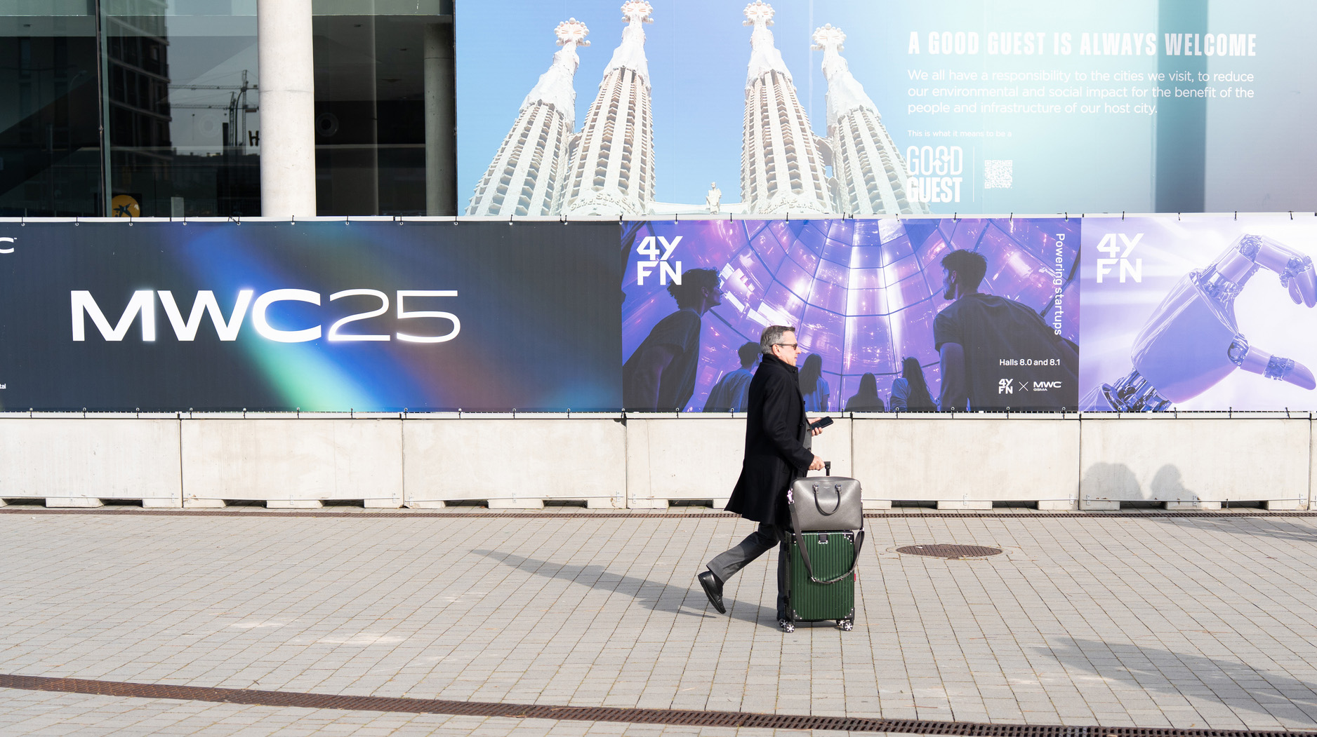 Immagine che rappresenta un uomo d'affari che cammina con la valigia al MWC di Barcellona, ​​passando davanti alla pubblicità dell'evento